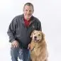 Man kneeling beside a happy golden retriever on a leash, studio background.