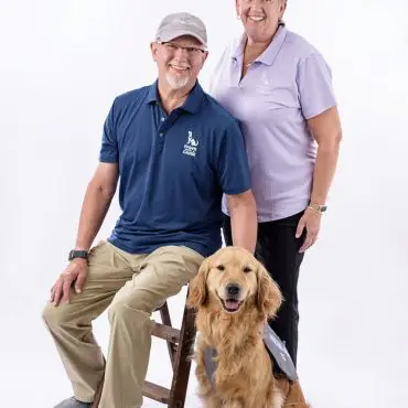 Man and woman smiling with a golden retriever in Paws 4 A Cause shirts, studio portrait.