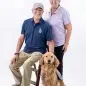 Man and woman smiling with a golden retriever in Paws 4 A Cause shirts, studio portrait.