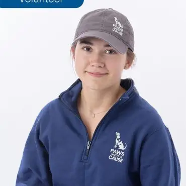 Volunteer wearing Paws with a Cause cap and pullover, smiling against a white background.