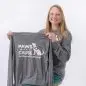 Smiling woman holds a Paws with a Cause shirt, promoting assistance and facility dogs.