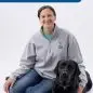 Smiling woman in grey sweater with black Lab on white background, Paws for a Cause logo visible.