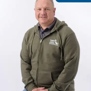 Man in olive hoodie sitting on stool, with Paws with Cause logo; Chris Staff text in upper right corner.