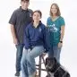 Group with a service dog wearing Paws With A Cause shirts, posing together. White background.