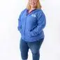 Woman in blue hoodie and jeans smiling, standing against a white background.
