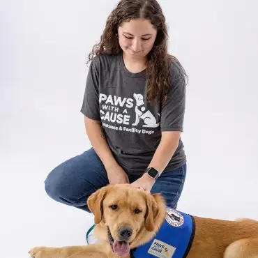 Woman kneeling next to a service dog in a Paws With A Cause vest, on a white background.