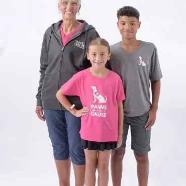 Three people smiling, wearing Paws with a Cause shirts, against a white background.