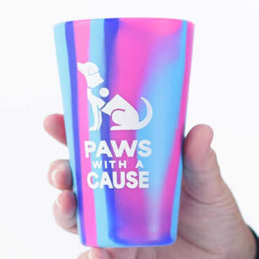 Colorful Paws With a Cause cup held in hand, featuring a dog logo on a pink and blue background.