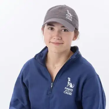 Person wearing Paws with a Cause gear, dark gray cap, and blue sweatshirt, smiling, against a white background.