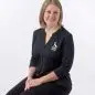 Smiling woman in a black Paws with a Cause shirt sitting on a wooden stool against a white background.