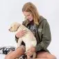 Girl in casual wear sitting, holding a yellow lab puppy on her lap against a white background.