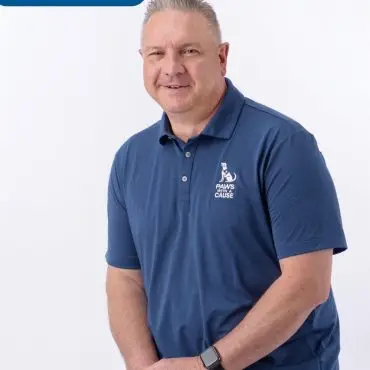 Man in blue polo with Paws With a Cause logo, seated, white background. Text reads Chris Staff.
