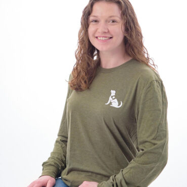 Smiling person wearing green dog-themed shirt and jeans, isolated on white background.