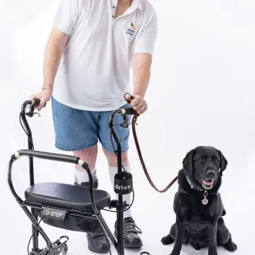 Man with mobility aid and black dog on a leash, smiling for a portrait.