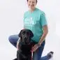 Woman kneeling with a black Labrador wearing a service dog tee, on white background.