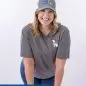 Smiling woman in a Paws for a Cause cap and grey shirt, leaning on a stool.