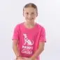 Young girl in a pink Paws with a Cause t-shirt smiles while leaning on a wooden stool.