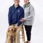 Elderly couple with a golden retriever dog, wearing Paws Cause sweaters, smiling in a studio portrait.
