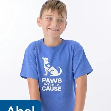 Young volunteer smiling in a Paws With a Cause shirt, standing with hands on a stool.