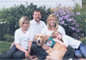 Family posing with their therapy dog in garden with colorful flowers.
