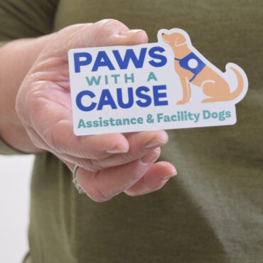 Hand holding Paws With A Cause sticker for assistance and facility dogs charity.