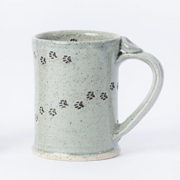 Grey ceramic mug with paw print design, speckled texture, and large handle, isolated on white background.
