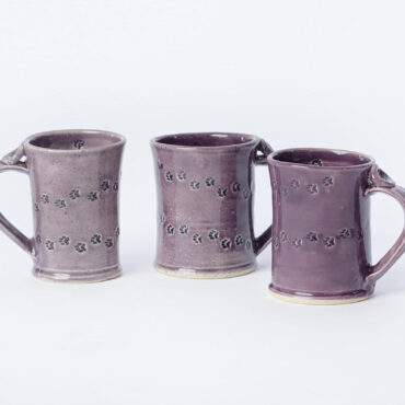 Three purple ceramic mugs with paw print design on a plain background.