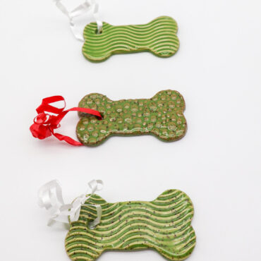 Three green bone-shaped ornaments with textured patterns and colorful ribbons on a white background.