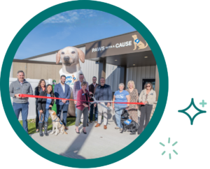 Group smiles at Paws With a Cause opening, large dog statue, ribbon cutting, service dogs present.