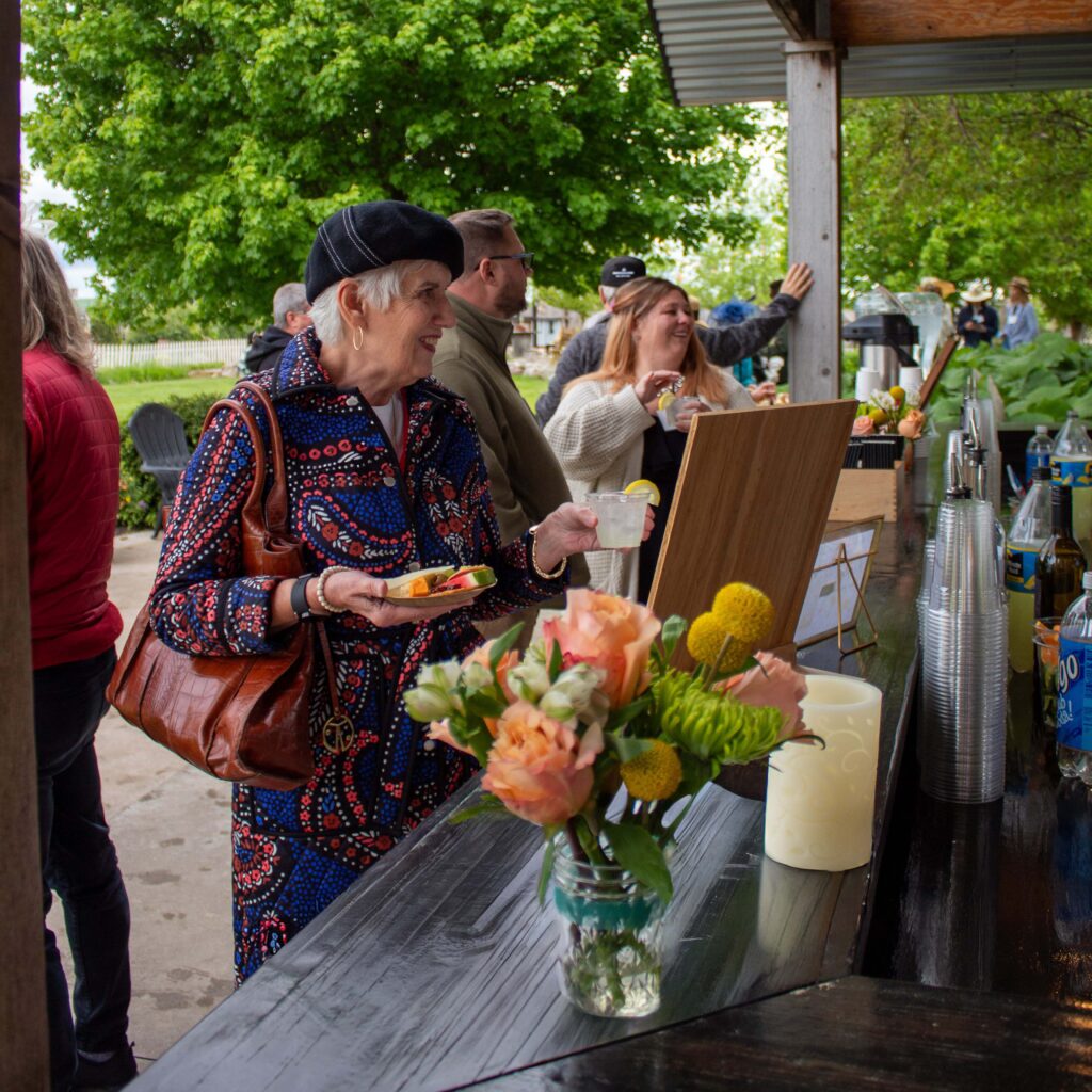 Group of people enjoying drinks and snacks outdoors at a bar with vibrant flowers in the foreground.