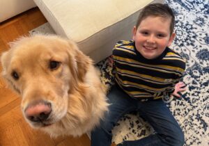 Boy smiling on carpet with a Golden Retriever. Cozy home vibe.