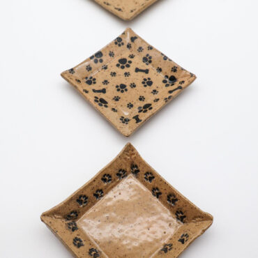Three square ceramic plates with black paw and bone patterns, arranged vertically on a white background.