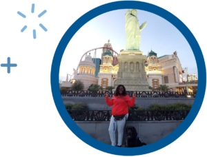 Woman with dog at Statue of Liberty replica, wearing red sweatshirt, Las Vegas backdrop, evening setting.
