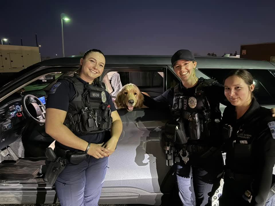 Police officers and a happy dog near a patrol car at night, showcasing teamwork and community spirit.