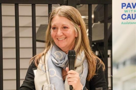 Smiling woman holding a microphone, speaking at an event.