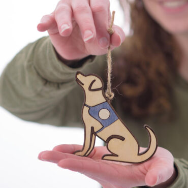 Person holding handmade wooden dog ornament with a string, smiling in the background.