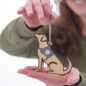 Person holding handmade wooden dog ornament with a string, smiling in the background.