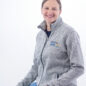 Smiling person in a gray jacket with Paws for a Cause logo, sitting on a stool against a white background.