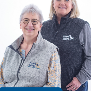 Two staff members from Paws With a Cause wearing logo vests, smiling in a portrait setting.