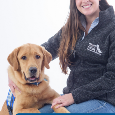 Young woman with service dog from Paws with a Cause organization, sitting together, both smiling at the camera.