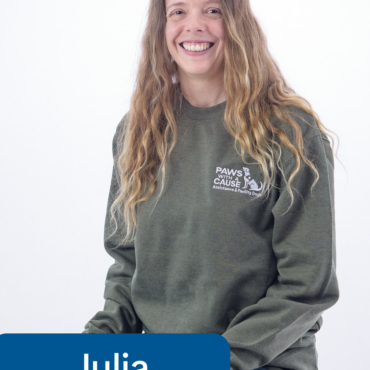 Smiling woman in a Paws With A Cause sweatshirt with Julia, Staff label, on a white background.