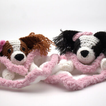 Two handmade crochet dog toys with pink bows, nestled in a fluffy blanket. Perfect gift for dog lovers.