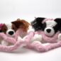 Two handmade crochet dog toys with pink bows, nestled in a fluffy blanket. Perfect gift for dog lovers.