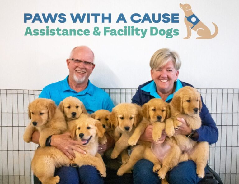 Couple smiling with a litter of golden retriever puppies for Paws With A Cause Assistance & Facility Dogs program.