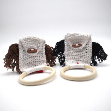 Crocheted baby teething rings with handles and tassels, in white, brown, and black yarn, on a white background.