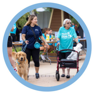Woman with a golden retriever assists an elderly lady with a walker at a charity event, Paws With a Cause.
