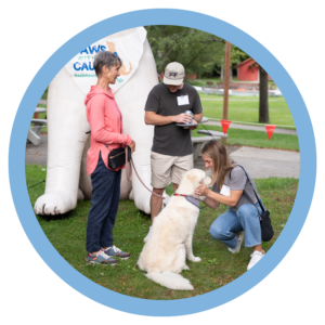 People interacting with a friendly dog at an outdoor event, with a Paws with a Cause banner in the background.