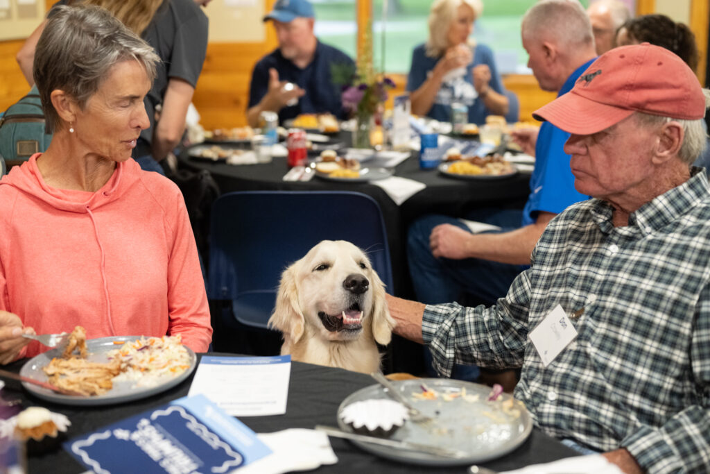 Golden retriever at dinner table with people, smiling and enjoying company at a social gathering.