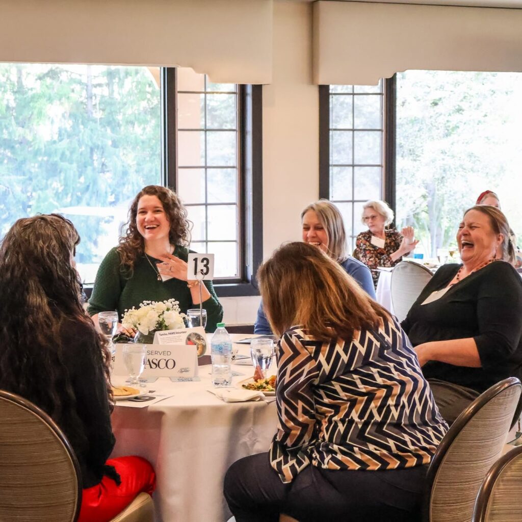 Group of women enjoying a lively conversation at a round table during a social event indoors.