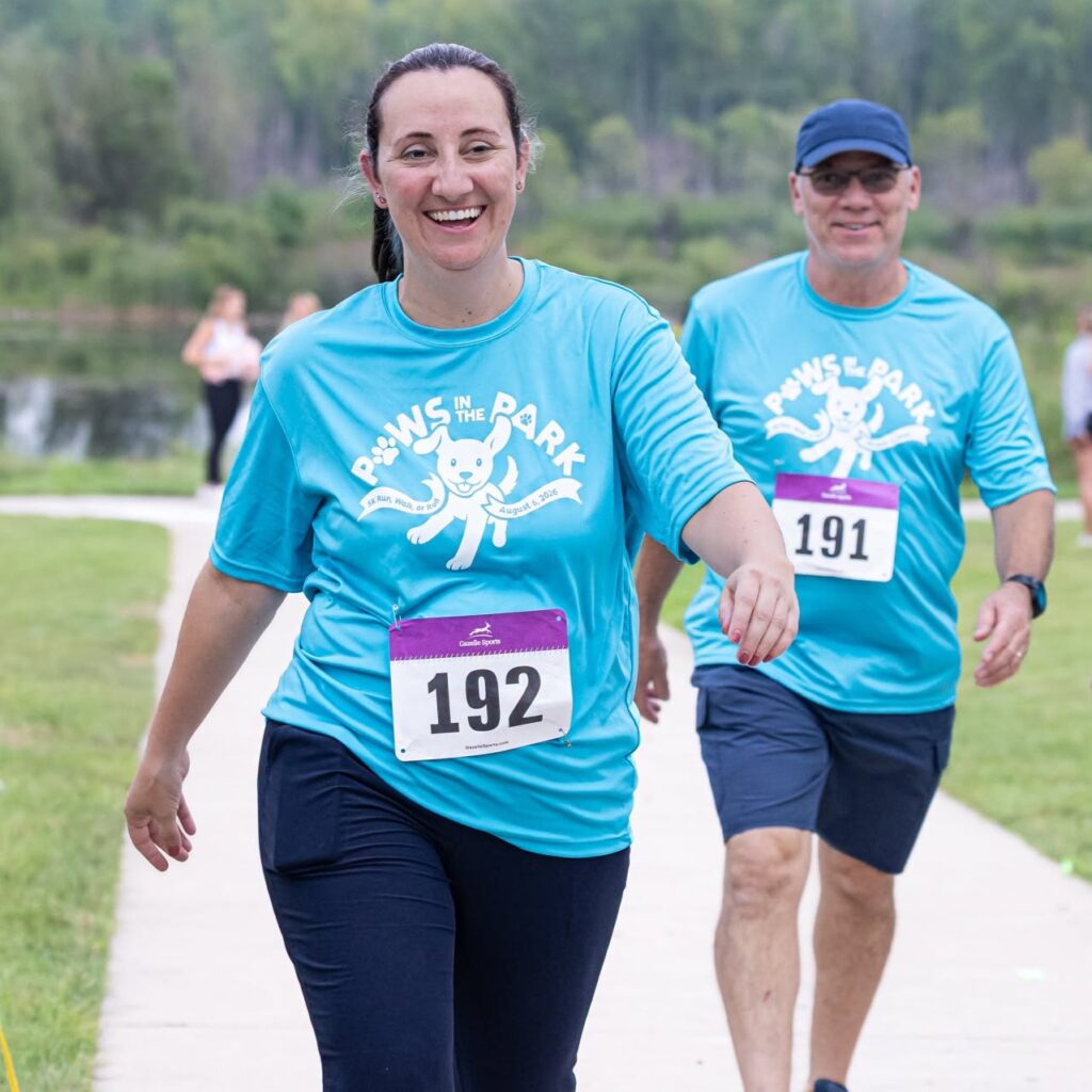 Participants in blue Paws in the Park shirts walking at a charity event, bibs 192 and 191, smiling outdoors.